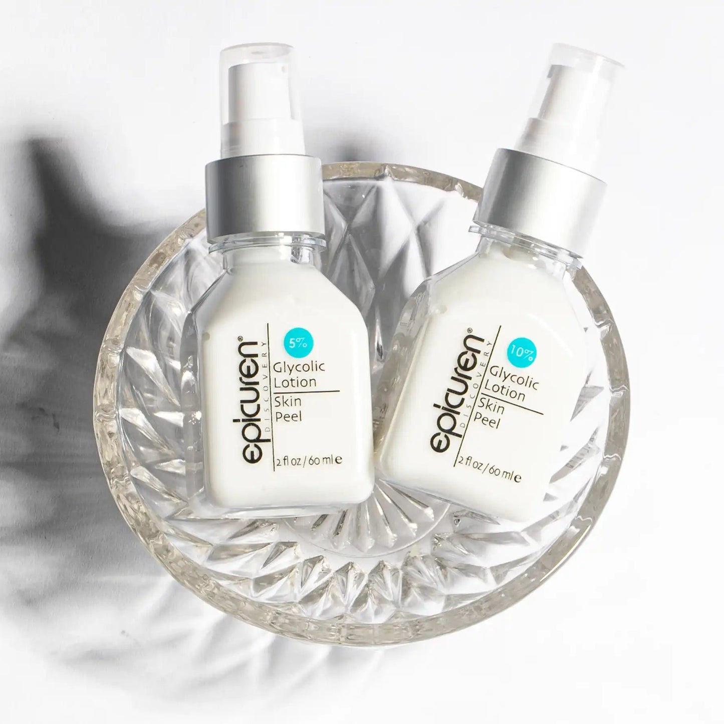 Two bottles of Epicuren Glycolic Lotion on a decorative glass plate with a white background.