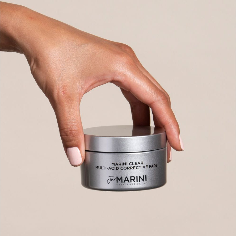 Hand holding a jar of Marini Clear Multi-Acid Corrective Pads against a beige background