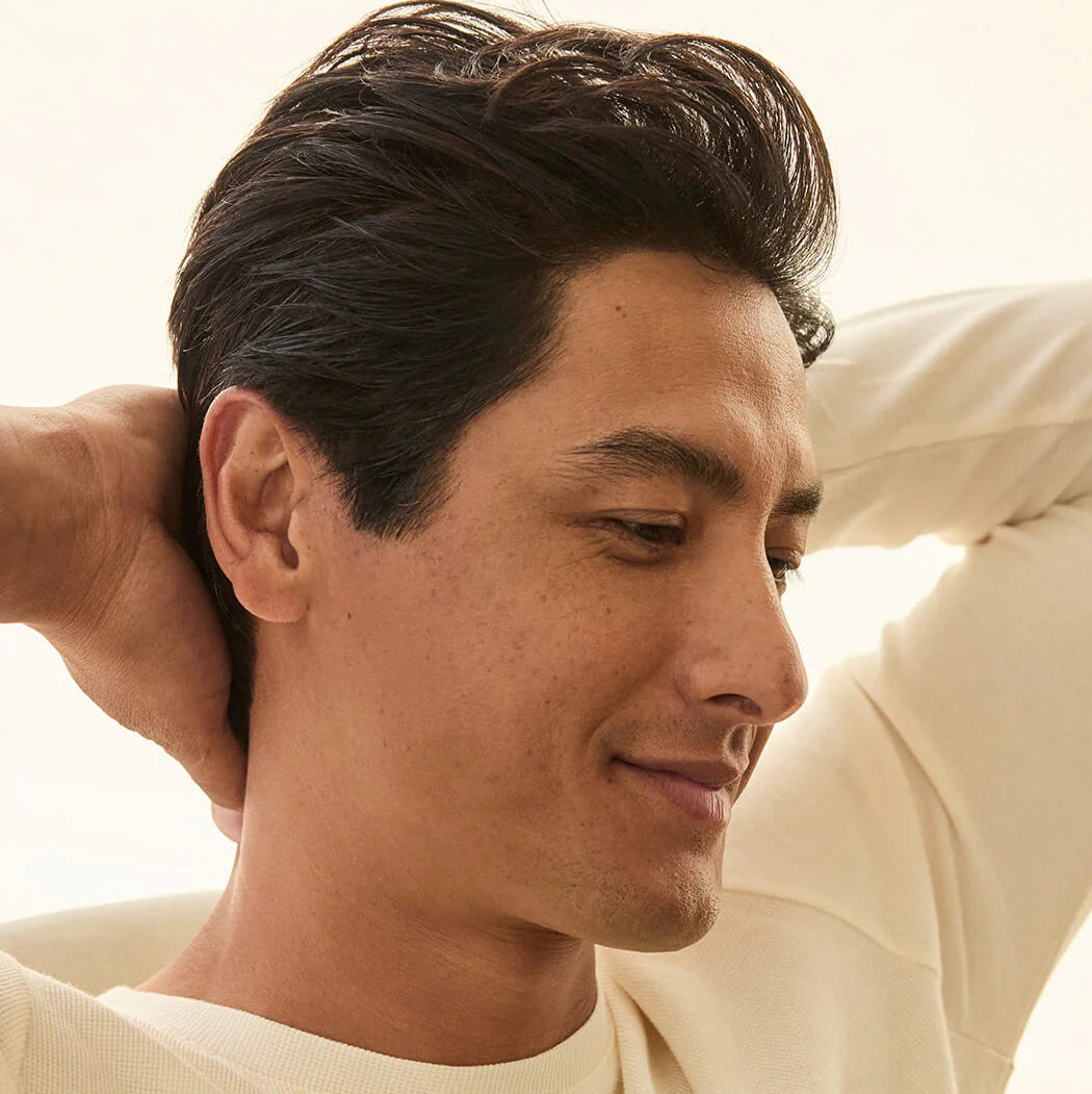 Man with dark hair wearing a white garment against a neutral background