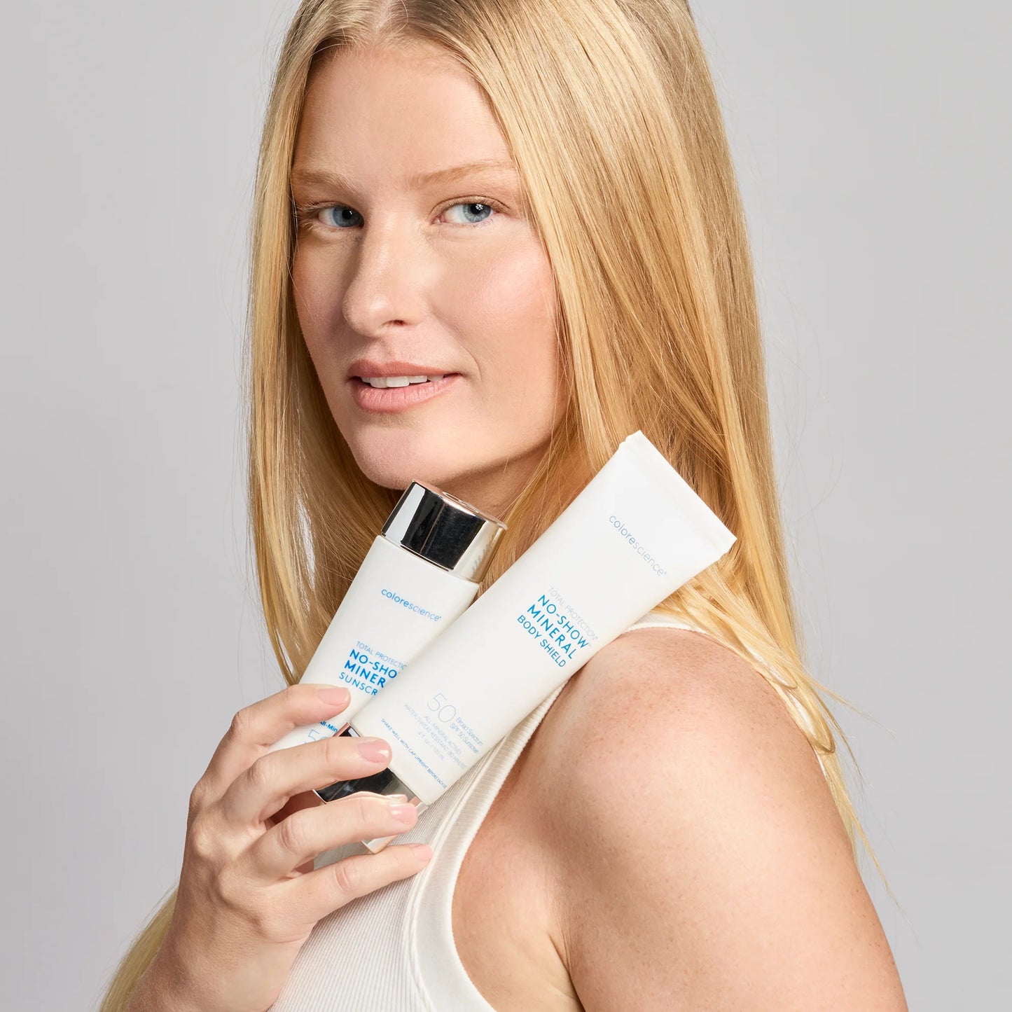 Woman holding two skincare products against a gray background