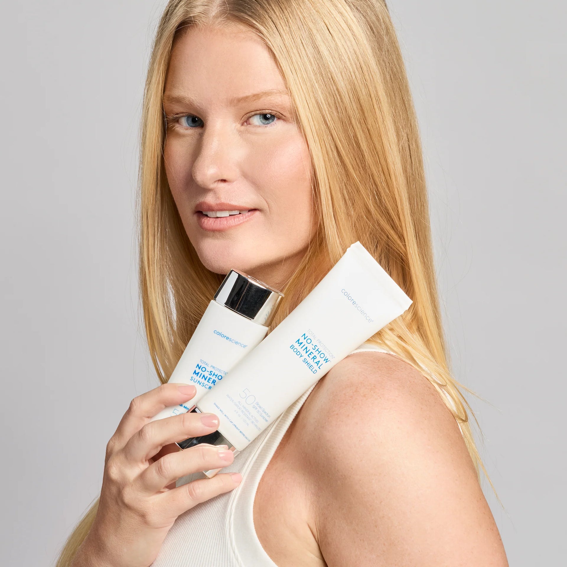 Woman holding two skincare products against a gray background