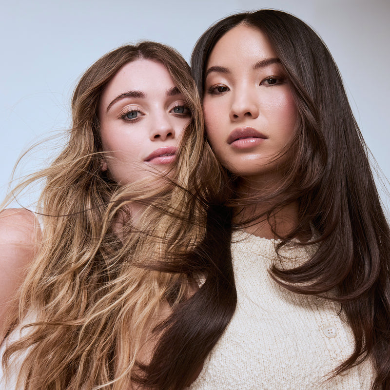 Two women with long, wavy hair posing against a plain background