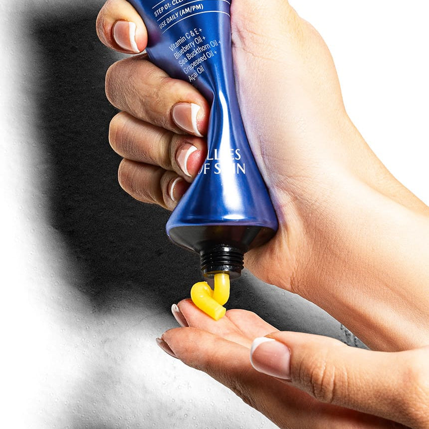 Hand holding a blue tube of vitamin C and omega cleansing balm, with a close-up of the balm being squeezed out.