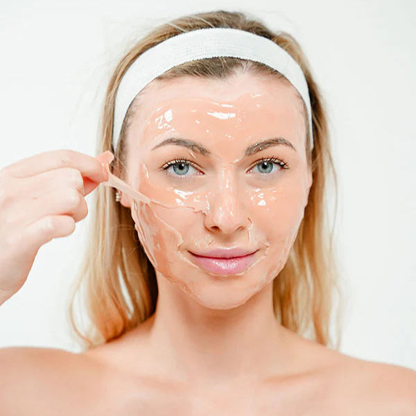 Woman applying a face mask with a white headband on a plain background