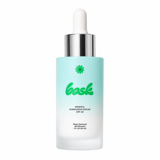 A frosted glass bottle of bask Mineral Sunscreen Serum SPF 30 with a light blue gradient body, green logo, and a white dropper cap on a white background. - Bask Mineral Sunscreen Serum - SPF 30