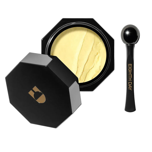 Eighth Day Overnight Eye Cream : An open black octagonal makeup compact showing a pale yellow pressed powder, with the matching lid placed beside it and a small black applicator spoon on a clean white background.