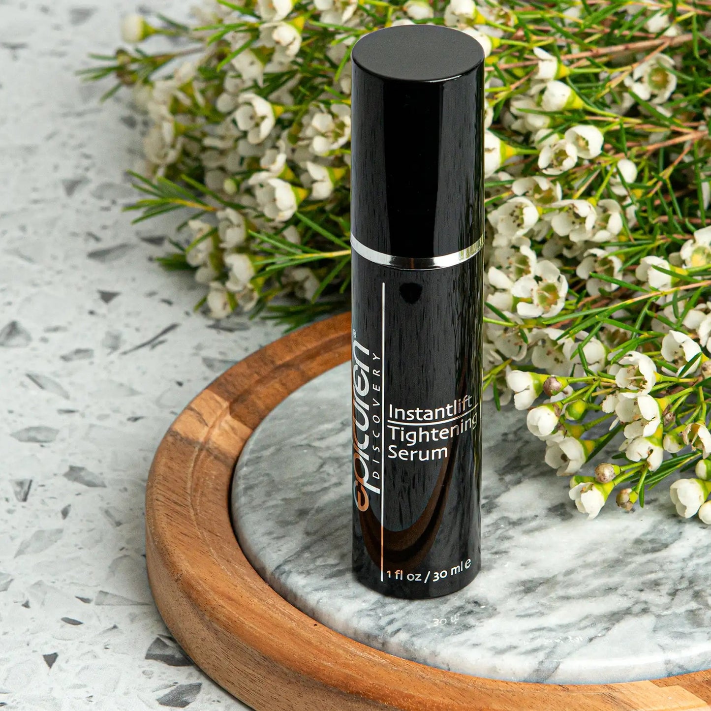 Black serum bottle on a marble surface with flowers in the background