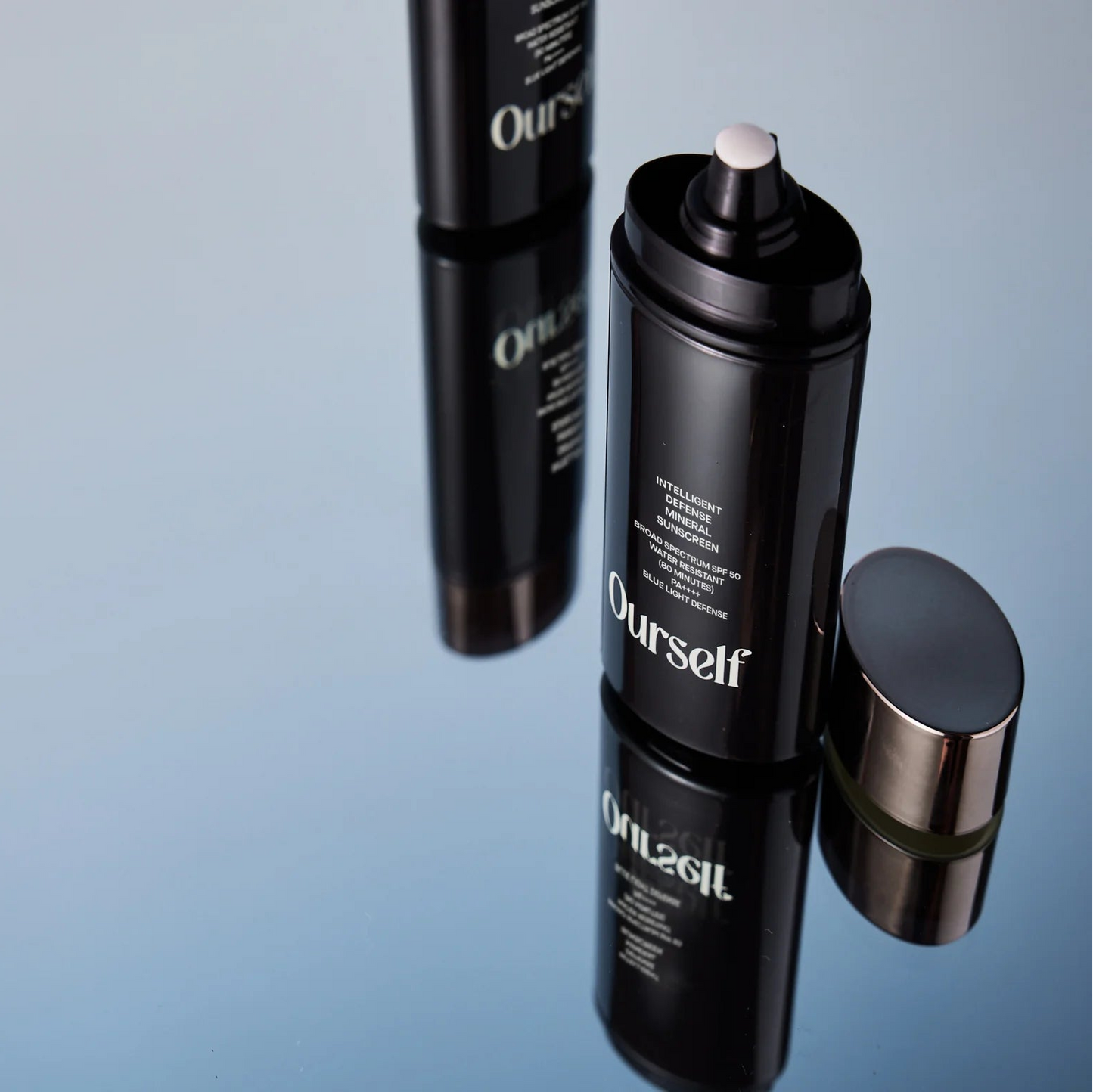Black cosmetic bottles with 'Ourself' branding on a reflective surface.