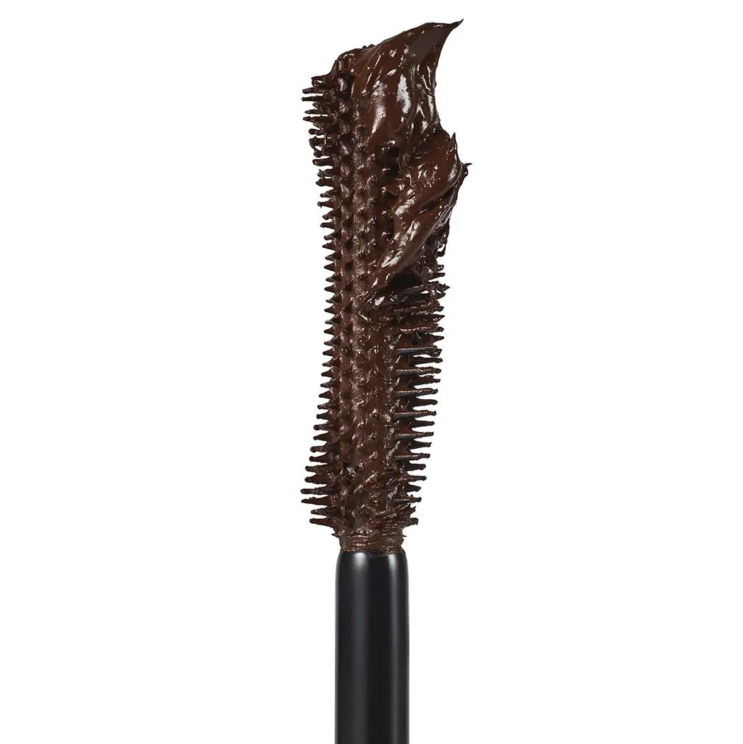 A close-up of a mascara wand showing a thick, glossy dark brown formula coated on the bristles, set against a solid white background.