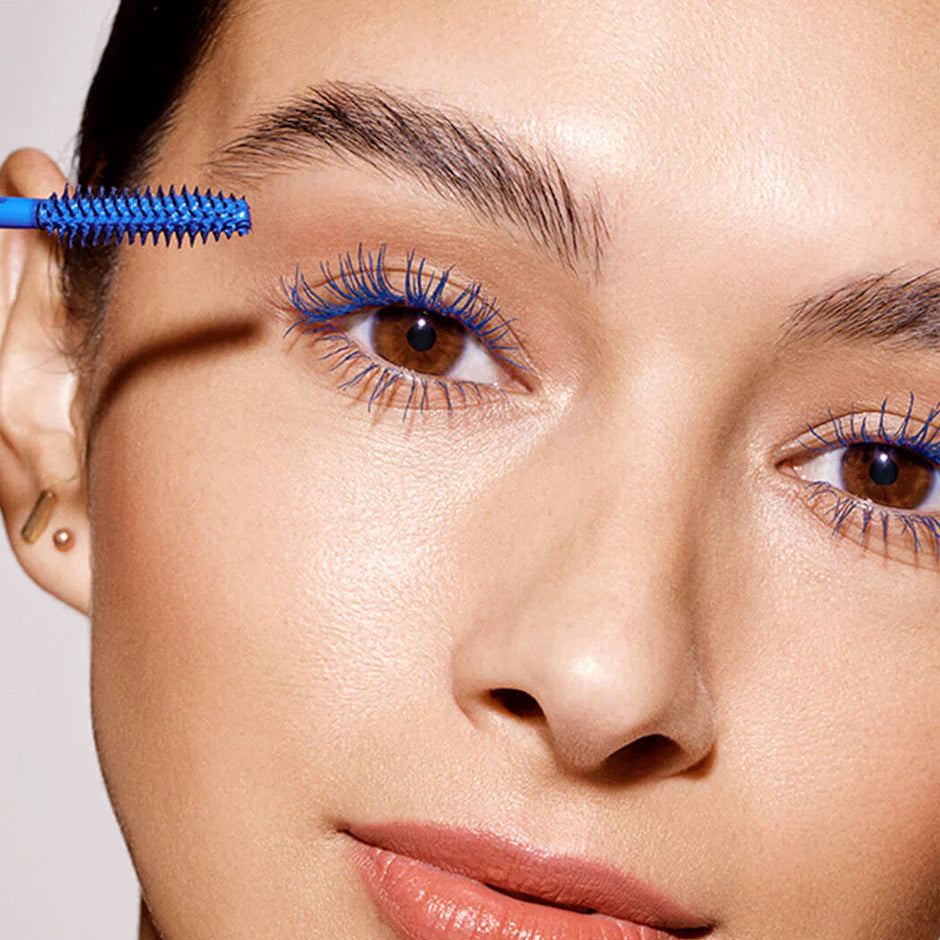 Close-up of a woman applying blue mascara to her eyelashes with a brush.