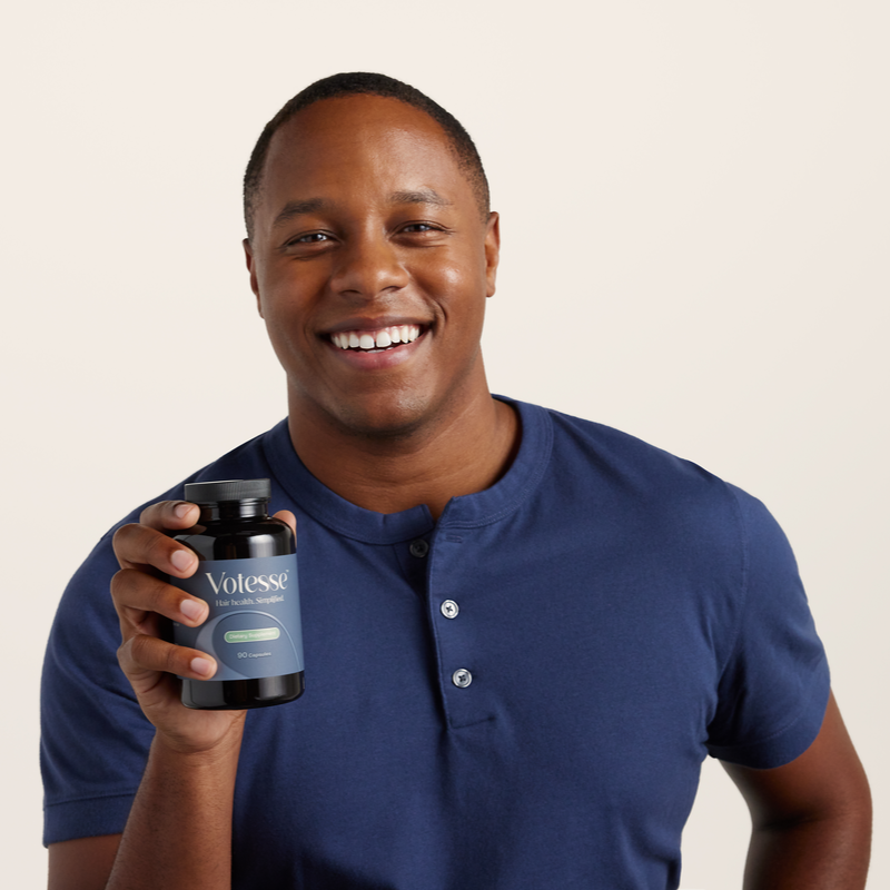 Man holding a bottle of Votess supplements against a plain background