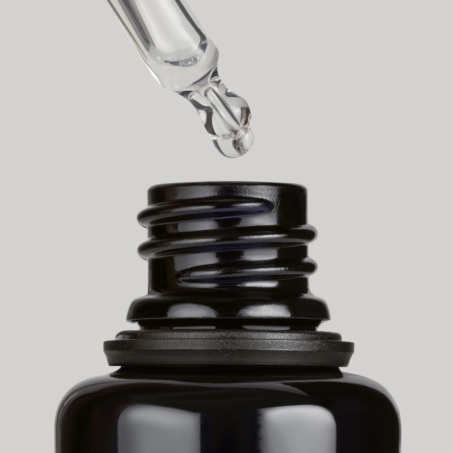Black dropper bottle with a droplet of liquid on a gray background