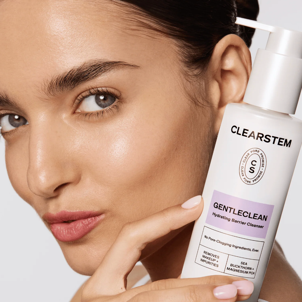 Woman holding a bottle of Clearstem GentleClean cleanser against a neutral background