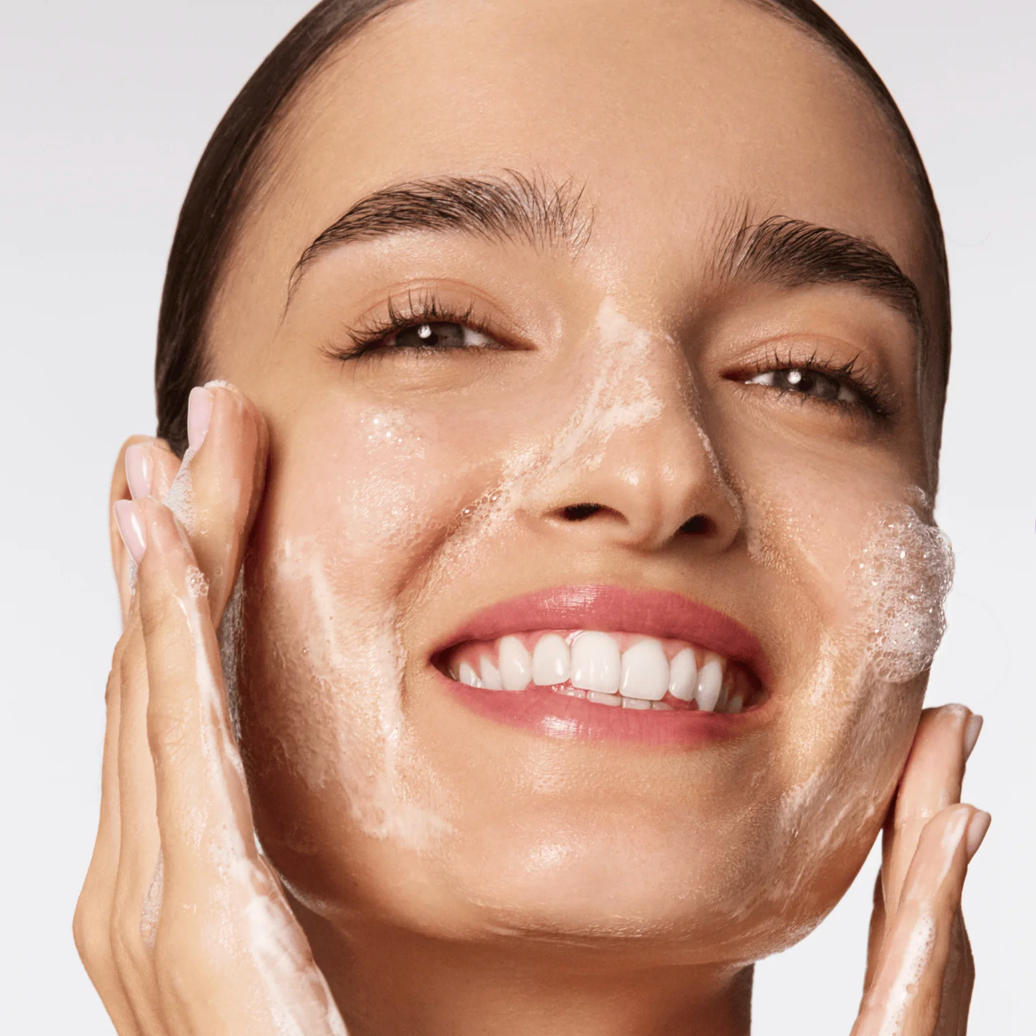 Woman applying a skincare product to her face with a neutral background.