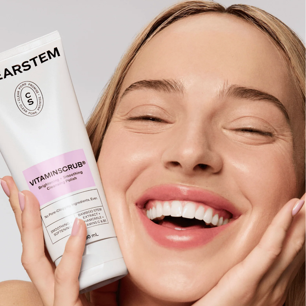 Woman holding a Clearstem Vitamin Scrub bottle against a neutral background