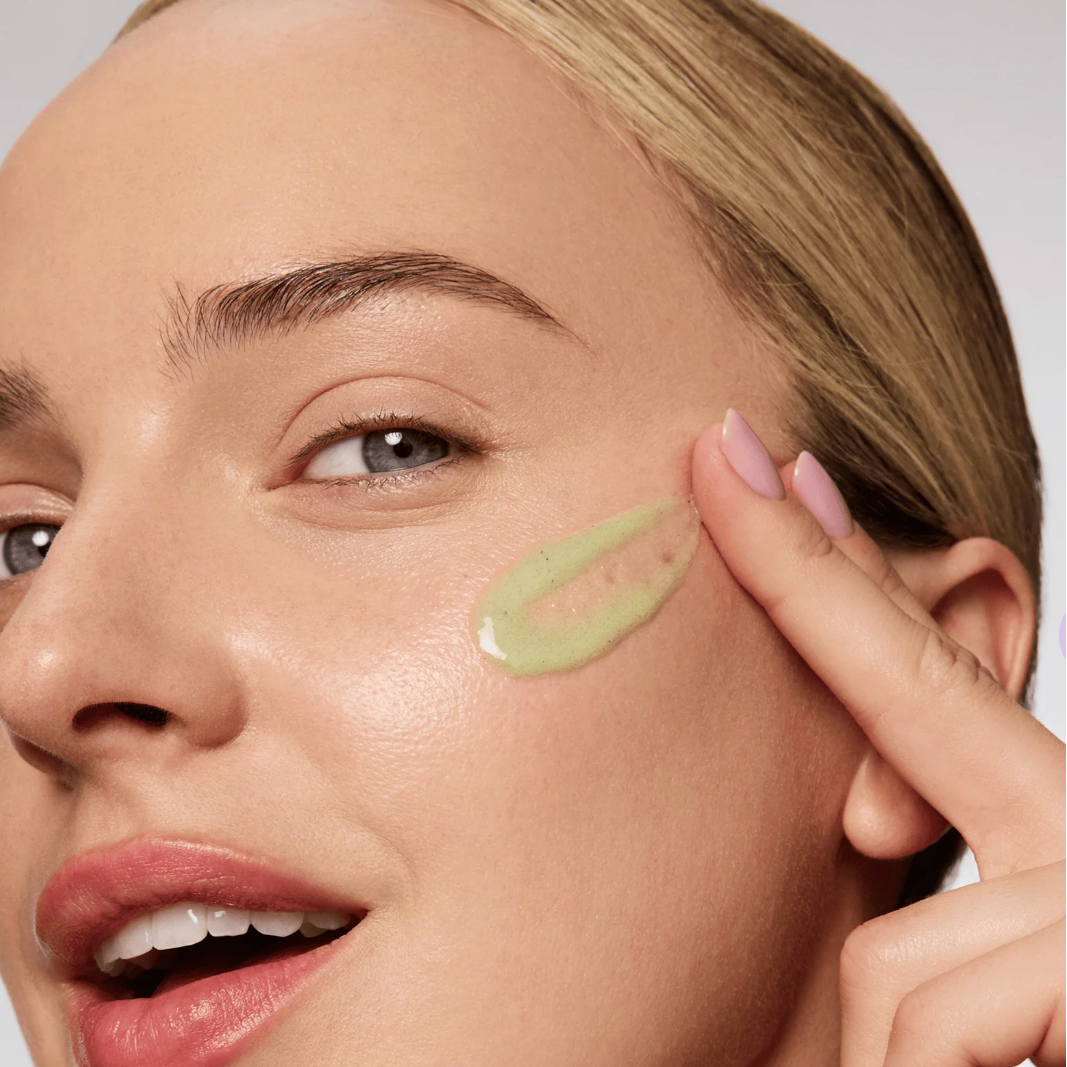 Woman applying green cream to her face with a neutral background