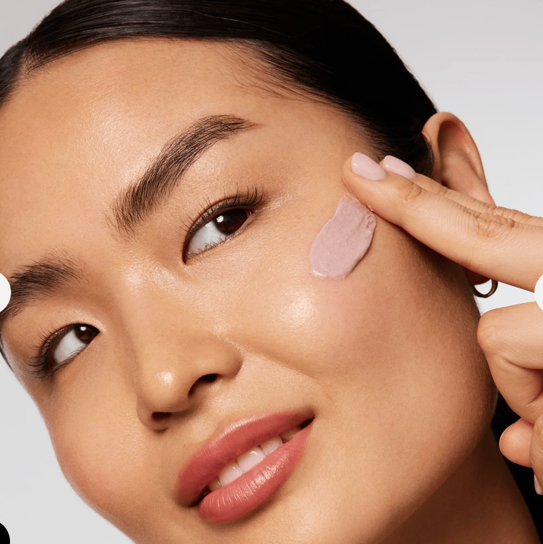 Close-up of a woman applying skincare product to her face with a cotton pad.