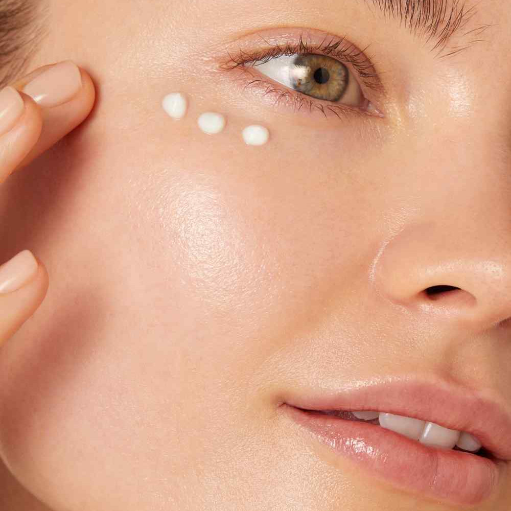 Close-up of a person applying cream under their eye.