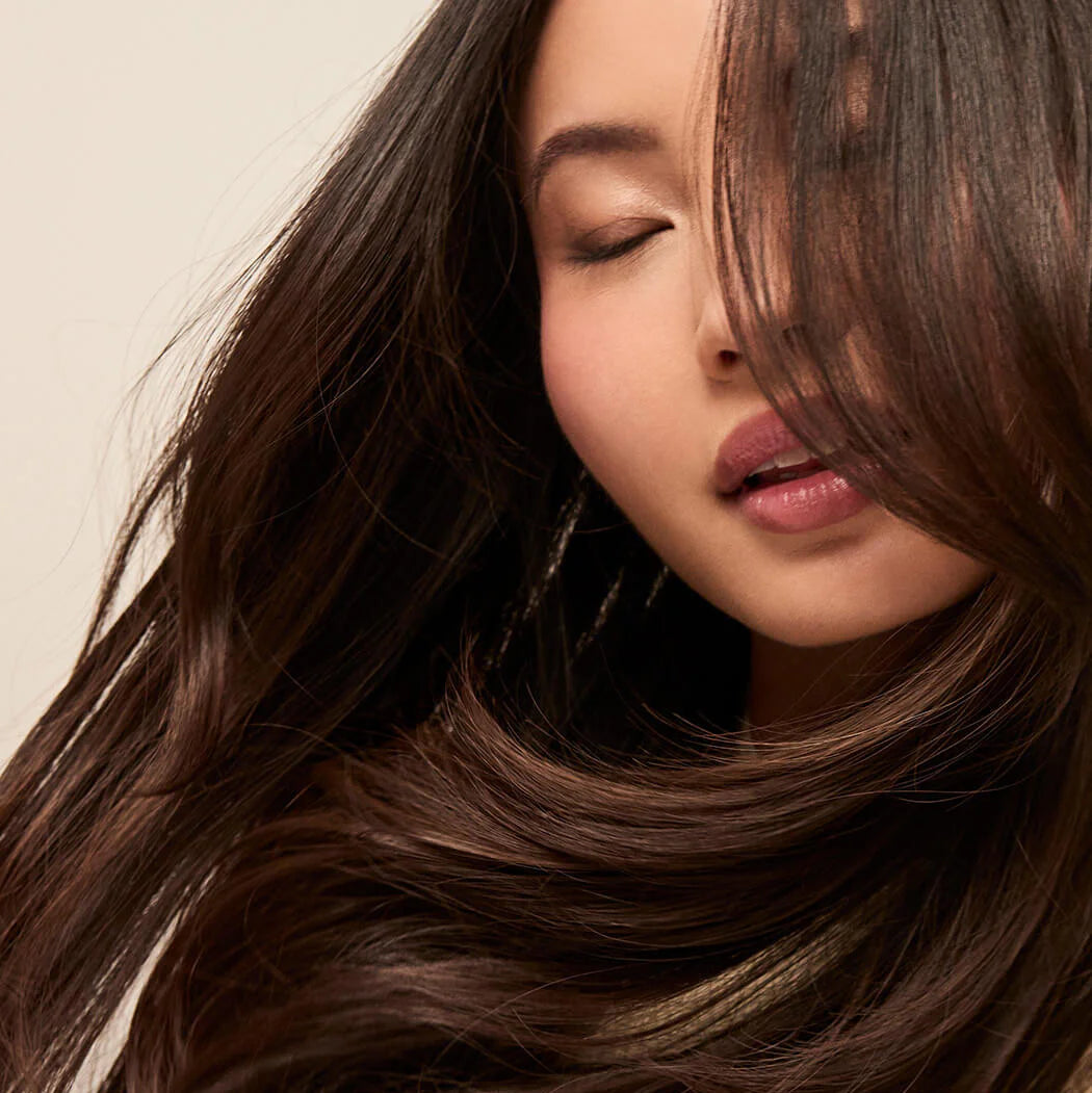 Close-up of a person with long, wavy brown hair against a neutral background