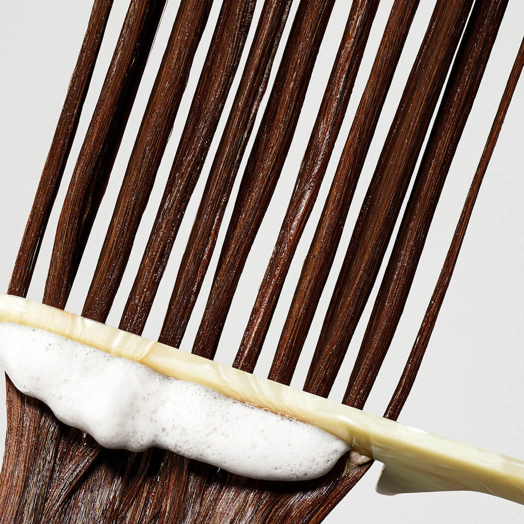 Close-up of a hairbrush with brown hair and white conditioner on a light gray background