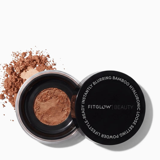 An open black FitGlow Beauty setting powder compact showing a shimmering bronze-brown powder, with loose matching powder scattered to the left on a clean white background.